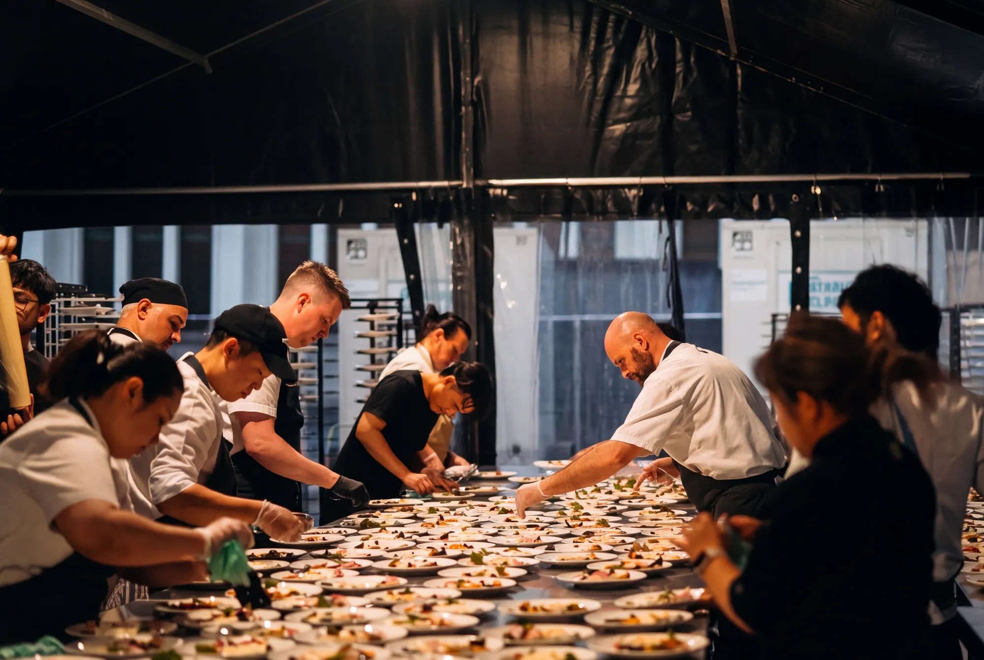 Kitchen team plating hundreds of entrées on one long bench